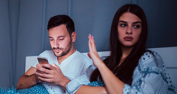 Pareja en la cama. él con su celular